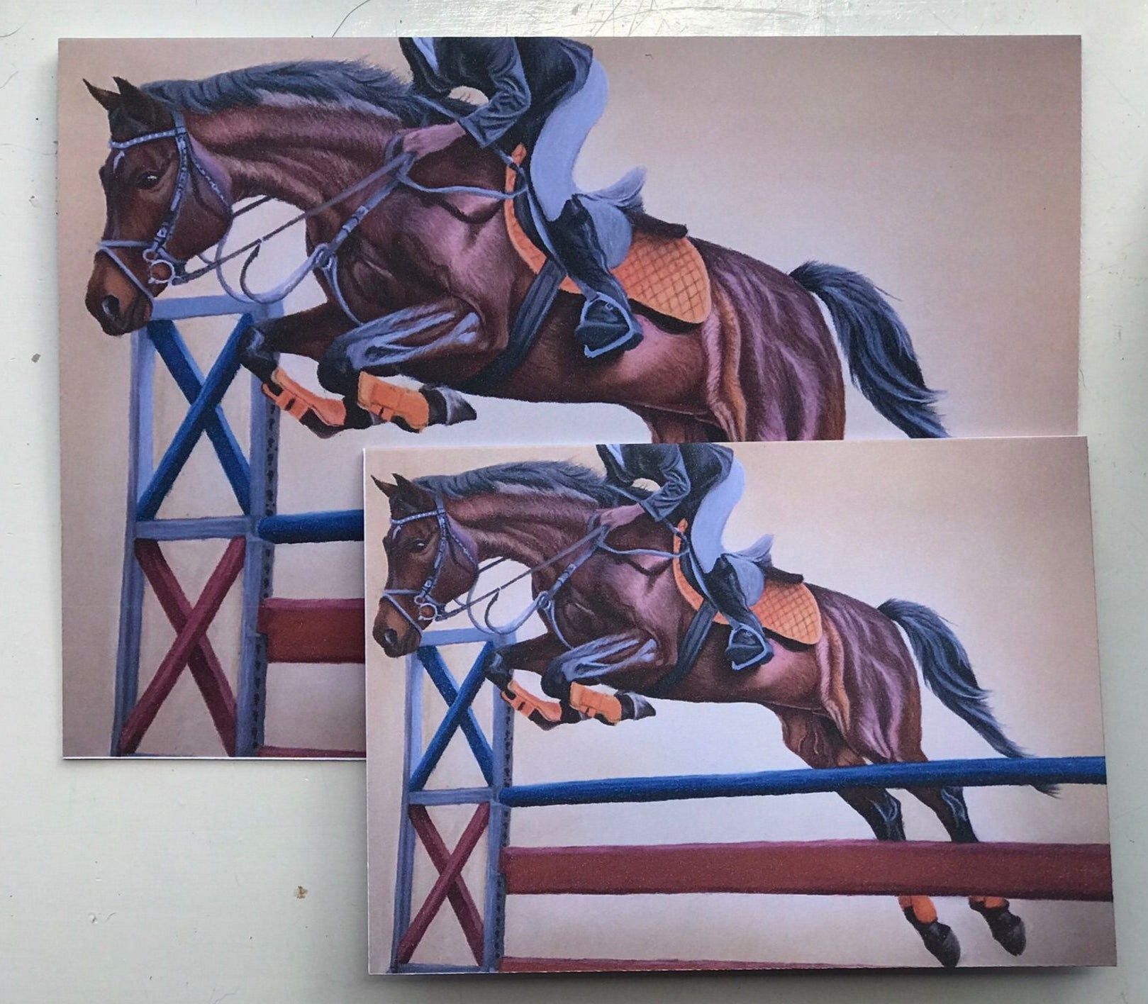 Two sized greeting cards with a drawing of a horse jumping over a fence on a beige background.