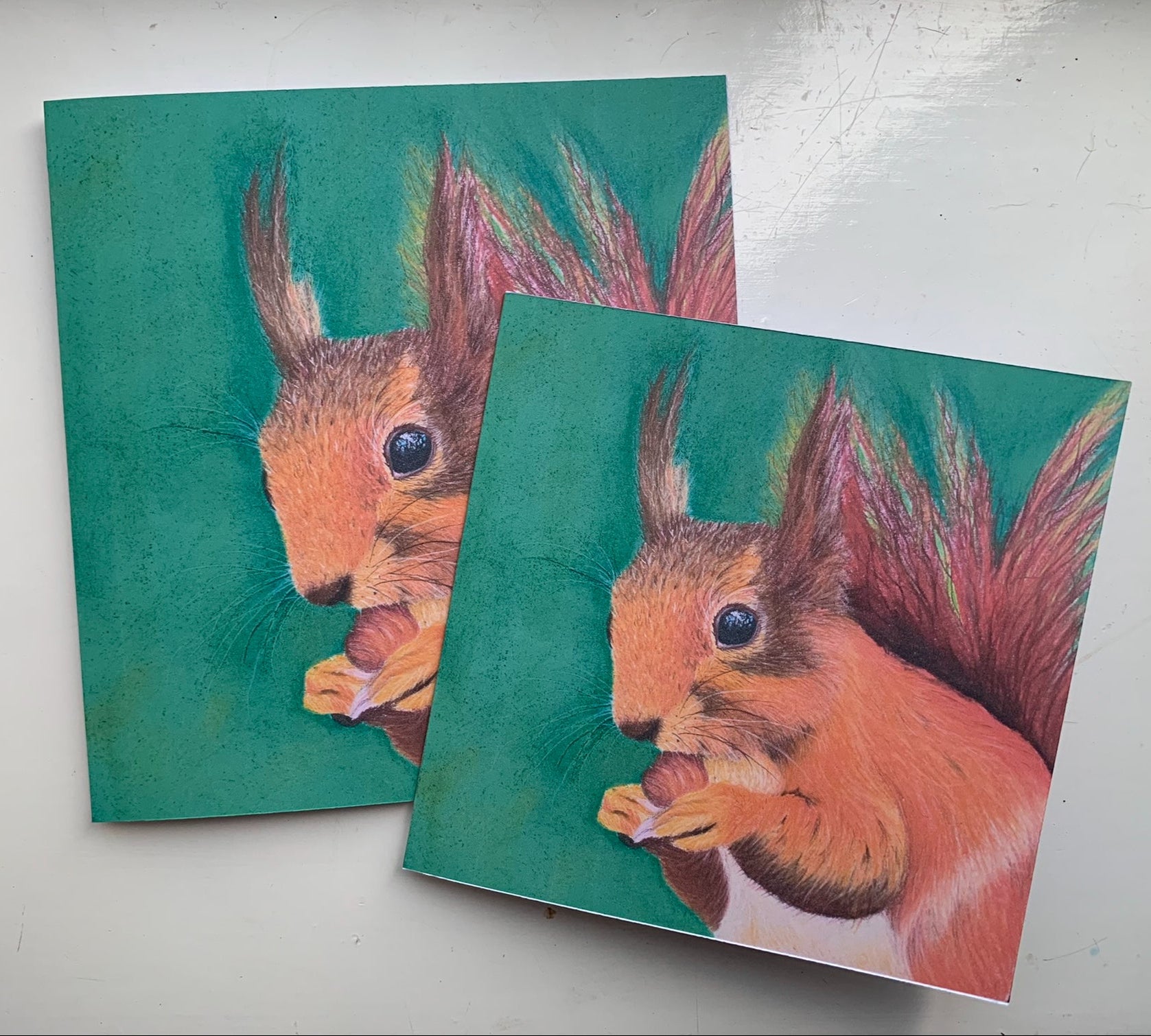 Two square cards with a red squirrel design on green backgrounds.